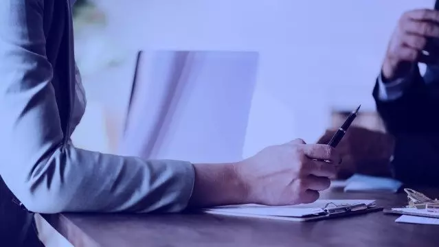 Pessoa segurando caneta apoiada sobre a mesa